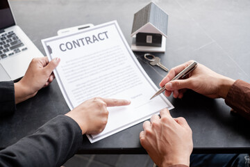 A real estate agent with a house model is talking to clients about buying home insurance and having customers sign contracts under the formal contract agreement. Home rental and insurance concept
