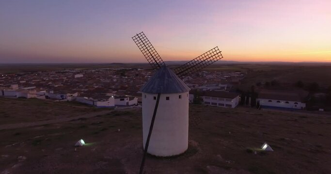 Aerial view Beautiful sunset over white cylindrical towers and pointed roofs of old Spanish windmills on background with Campo de Criptana, Spain
