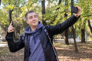 A male blogger in a leather jacket in the forest conducts a video conference for his audience. The concept of online learning, master classroom and video blogging.