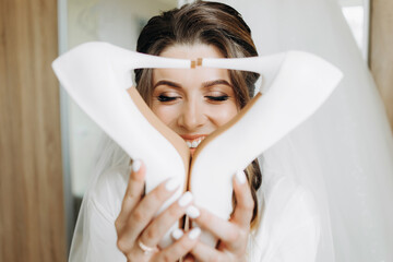 Fototapeta premium Cute girl with closed eyes holds her wedding shoes in her hands in front of her face
