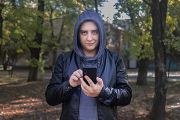 Concept. A man in a leather jacket with a hood looks at the phone and smiles like a maniac or a...