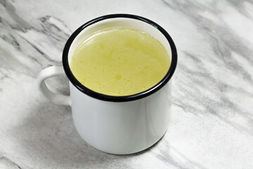 Chicken broth in a white mug on a gray marble table. Meat broth. Healthy food. Broth for the disease. Close-up.