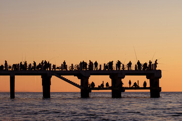 Silhouettes of the people fishing and enjoying the sunset over sea on a pier