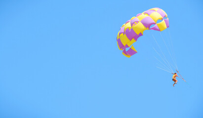 Multicolored parachute against the blue sky. Parasailing in summer. Woman under parachute hanging...