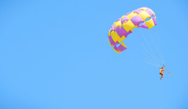 Multicolored parachute against the blue sky. Parasailing in summer. Woman under parachute hanging mid air.  Positive human emotions and feelings  , copy space
