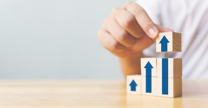 Hand arranging wood block stacking as step stair with arrow up. Ladder career path concept for business growth success process