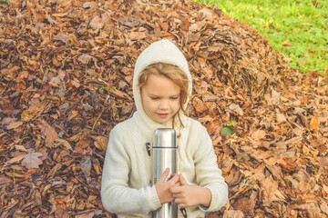 a autumn day child with a thermos on the background of fallen leaves