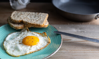 Fried organic egg sunny side up seasoned with salt and pepper on a plate with whole grain bread on the side.