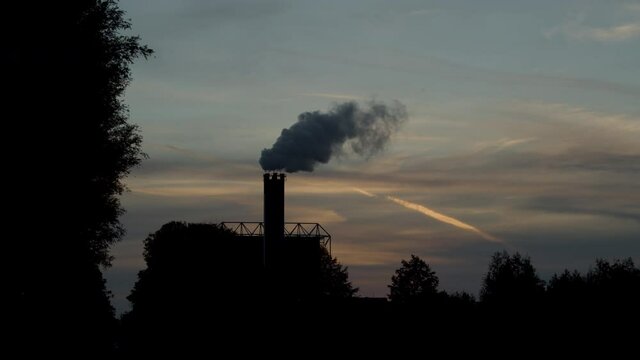 Beautiful silhouette of smoking factory chimney against a sunset in slow motion