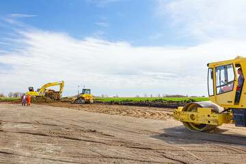 Excavator is loading a truck with ground on building site, road roller compact soil