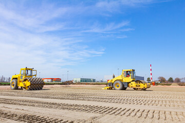 Two industrial rollers are compacting sand at construction site