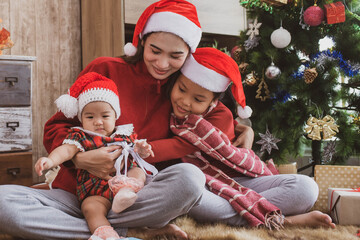 parent and two little children having fun and playing together near christmas tree indoors. merry christmas and happy holidays. cheerful mom and her cute daughters girls exchanging gifts.