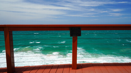View through a fence to the ocean. Red top rail of the fence is level with the horizon. 