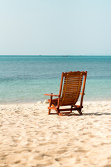 empty wooden deck chair by the sea. White sand and blue sea. Vacation, travel and tourism concept.