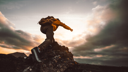 Hiker standing on the cliff mountain pointing the sky with fingers at sunset. Man on rocky cliff...