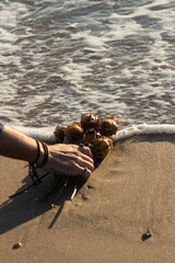 Mano de hombre con anillos y pulseras dejando ramo de flores rojas y blancas en la orilla del mar
