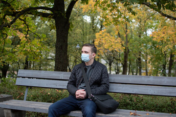 Obraz premium young adult guy sits on a park bench in dark clothes, green park autumn