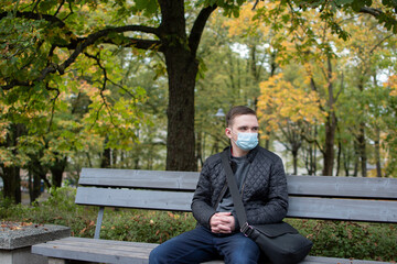 Fototapeta premium young adult guy sits on a park bench in dark clothes, green park autumn