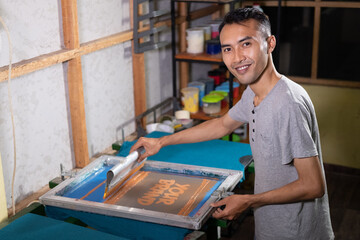 Male workers are confident in using the screen printing squeegee to print T-shirts at the workshop