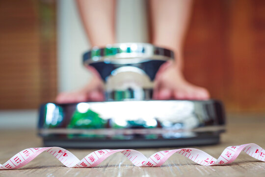 Tape Measure. Low Section Of Female Feet Stand Stepping On Electronic Scales For Weight Control On Floor. The Concept Of Slimming And Overweight Problem. Space For Text. 