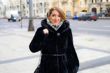 a beautiful young happy woman in fashionable winter fur coat walks along a city street