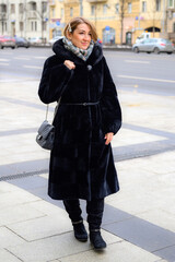 Fototapeta premium a beautiful young happy woman in fashionable winter fur coat walks along a city street