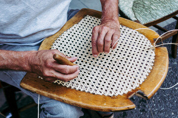 Close up sur les mains d'un artisan rempailleur de chaise en train de réparer une chaise en osier