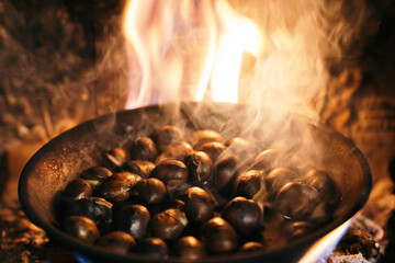 Chestnuts roasted in the chimney and smoking. Roasting chestnuts with a fire in the house. Celebrating the "Castanyada, Castañada" typical dish and tradition of Catalonia, Spain, in All Saints Day.