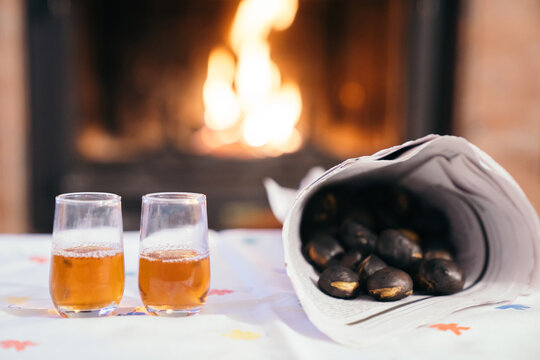 Celebrating "Castanyada" typical dish and tradition of Catalonia, Spain, in All Saints Day. Toasted chestnuts and two glasses with moscatell wine or liquor with the fire of fireplace at the bottom.