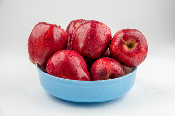 Pile of red apple in blue bowl with clear water drop on 
shell surface texture pattern isolated, white background