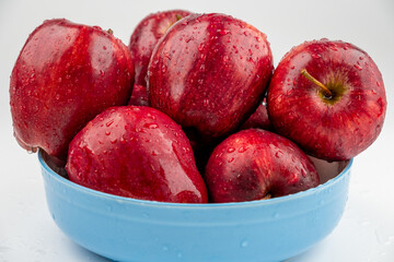 Pile of red apple in blue bowl with clear water drop on 
shell surface texture pattern isolated, white background