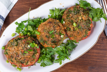 Provencal tomatoes - baked tomato halves with breadcrumbs and herbs on an oval dish, rustic background