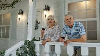 Senior elderly Caucasian couple drinking wine in porch at home. Happy mature retired family resting
