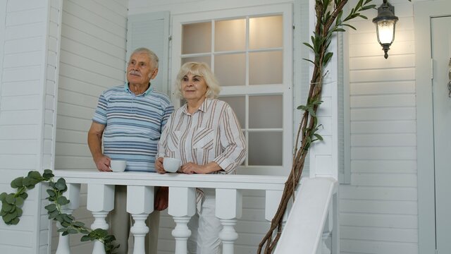 Senior Elderly Caucasian Couple Drinking Coffee, Looking Ahead In Porch At Home. Mature Family