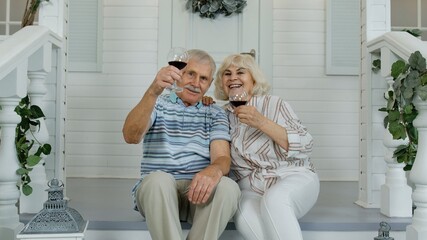 Satisfied senior elderly Caucasian couple sitting and drinking wine in porch stairs at home