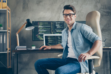 Portrait of positive guy it specialist sit chair desk enjoy working pc home ready debugging java script cyber space error wear denim jeans shirt in workplace