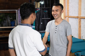 smiling Asian male owner shaking hands when meeting customers at the screen printing office