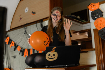 A girl in a Halloween make-up congratulates her friends and family on Halloween with a video call via a laptop. Celebrating at home a distance, online Halloween costume and mask contests