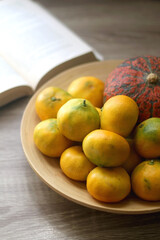 Wooden bowl with tangerines and a pumpkin and open book on a table. Selective focus.