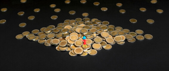 Miniature toy woman stands confidently on large pile of coins. Woman and money creative concept. Selective focus