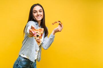 Pretty girl holds out a slice of pizza and looks at the camera with a smile. Yellow background. Place for text