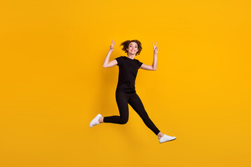 Fototapeta na wymiar Full length body size view of attractive funky cheerful girl jumping having fun showing v-sign isolated bright yellow color background
