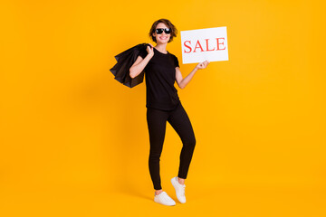 Fototapeta na wymiar Full length body size view of lovely cheerful girl carrying bags showing sale poster isolated bright yellow color background