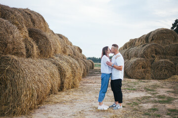 Naklejka na ściany i meble Lovers walk on a farm. A man and a woman are standing near haystacks. People are standing near haystacks. Farm.