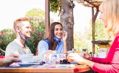 Happy friends with face mask drinking espresso at coffee house - New normal lifestyle concept of young people having fun at restaurant 