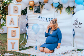 Baby shower - pregnant woman with a big tummy sits on the floor on a party setup