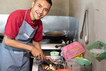 Cooks smile looking at cameras as they slice spices with knives and wood cutting boards in the kitchen