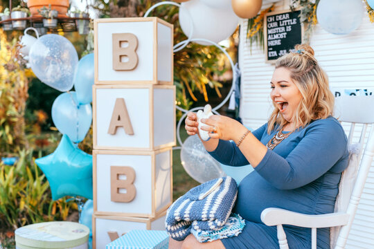 Pregnant woman sits on a Baby shower party setup and looking at the gifts, happy smiling, and exciting