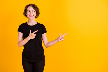 Portrait of attractive content cheerful girl pointing two forefingers aside copy space ad isolated bright yellow color background