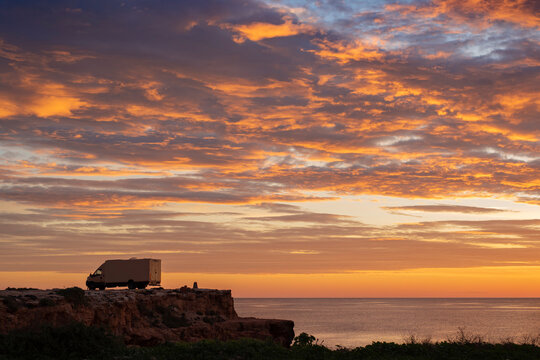 sunset / sunrise at rocky cliff with travel trailer above the sea. Dramatic and calm cloudy sky with sun beams